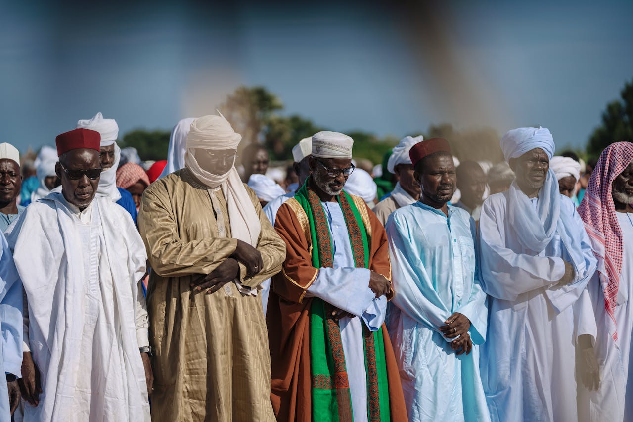 A group of men in traditional clothing pray together outdoors, showcasing religious and cultural diversity.